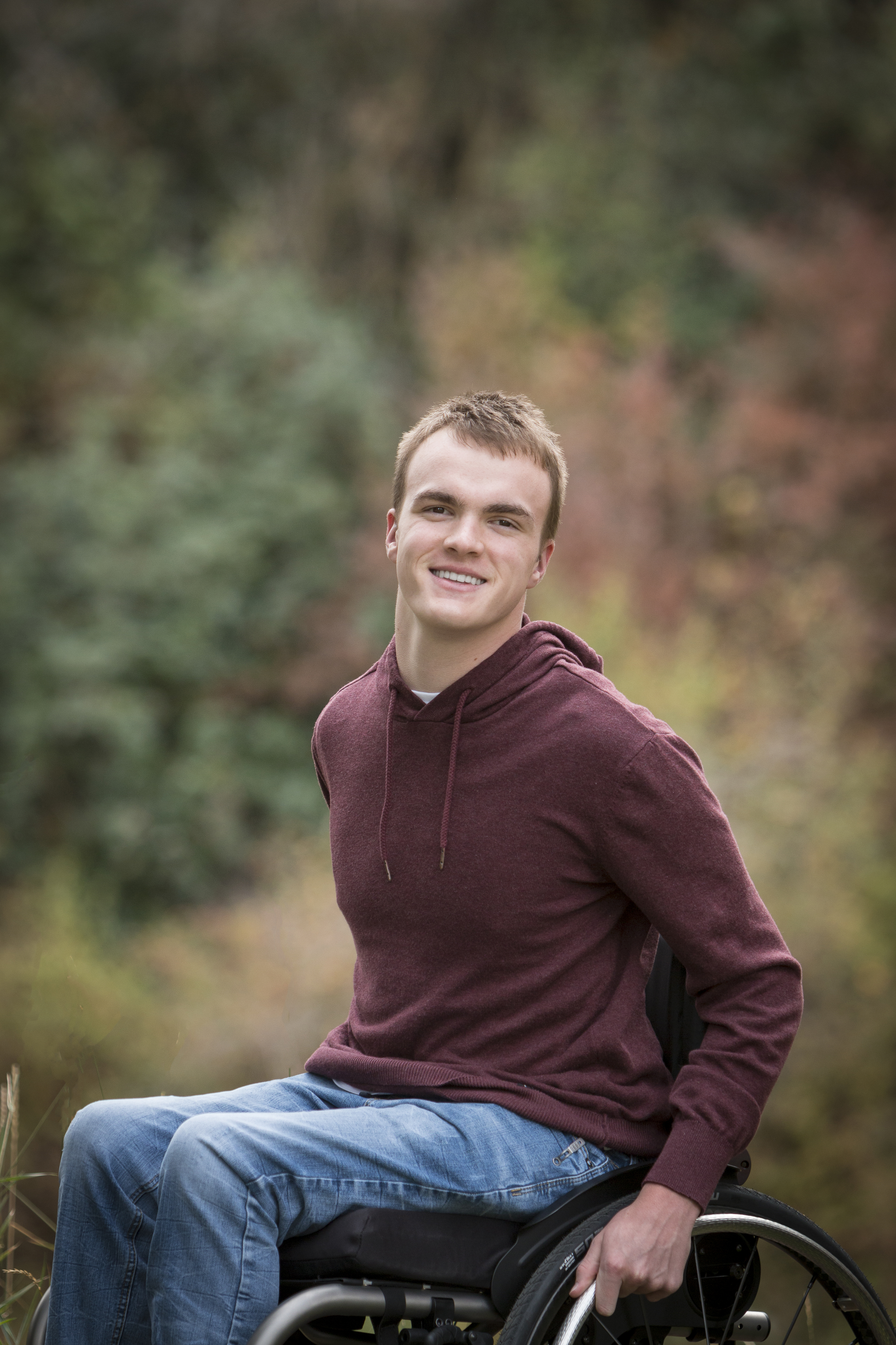 A photo of Hayden Stipe, wearing a red shirt and jeans while sitting in a wheelchair